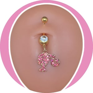 Könnte beinhalten: Goldfarbener Bauchnabelring mit einer hängenden rosa Strass-Silhouette. Der obere Ball und der untere Edelstein sind klar. Die Silhouette ist ein stilisiertes Bild eines Frauenkopfes.