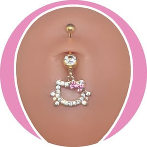 Puede incluir: Anillo para el ombligo dorado con un dije colgante de Hello Kitty. El dije está delineado con cristales transparentes y presenta un lazo rosa. Las gemas superior e inferior son claras y redondas.