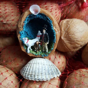 May include: A decorative walnut shell diorama with a miniature figure, dog, and monkey. The scene is set against a blue background, with a seashell below. Walnuts are visible in a red mesh bag, creating a unique display.