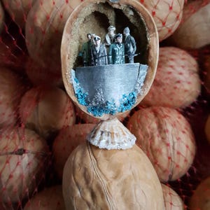 May include: A detailed walnut shell diorama with miniature figures on a platform, decorated with blue accents and a seashell base. The diorama is set against a backdrop of walnuts in a red mesh bag, creating a whimsical and detailed scene.