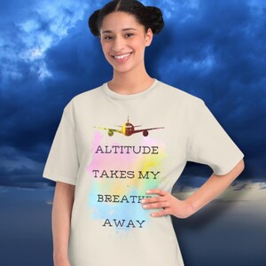 May include: A white t-shirt with a colorful watercolor design of an airplane and the text "Altitude Takes My Breath Away".