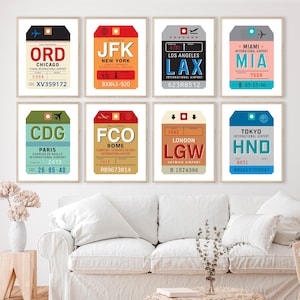 May include: Eight framed travel-themed art prints featuring vintage luggage tag designs. Each tag displays a different airport code, including ORD, JFK, LAX, MIA, CDG, FCO, LGW, and HND, with airport names and flight details.