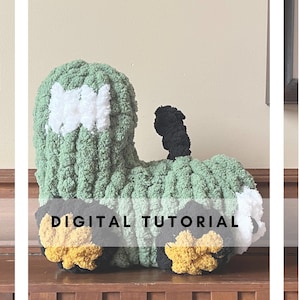 Peut inclure: Un train en crochet vert, blanc et noir avec des roues jaunes. Le jouet est sur une surface en bois et le texte "DIGITAL TUTORIAL" est sur l'image.