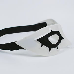 May include: A white eye mask with a black eye design and a black elastic band. The mask has a pointed shape and is likely for cosplay or costume use.