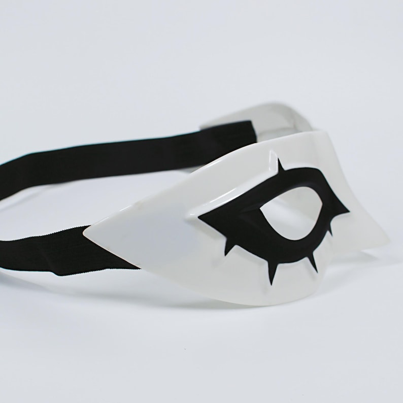 May include: A white eye mask with a black eye design and a black elastic band. The mask has a pointed shape and is likely for cosplay or costume use.