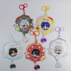 Op de afbeelding: Een verzameling van vijf sleutelhangers met anime-personages. Elke sleutelhanger heeft een cirkelvormig frame met een cartoonkarakterportret, omgeven door decoratieve elementen. De sleutelhangers zijn in verschillende kleuren, waaronder rood, geel, blauw en wit, met bijpassende sleutelringen.