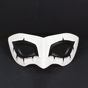 May include: A white mask with black eye coverings and sharp, pointed details. The mask has a smooth, glossy finish and is designed to cover the eyes and upper face. The mask is likely for costume or cosplay purposes.