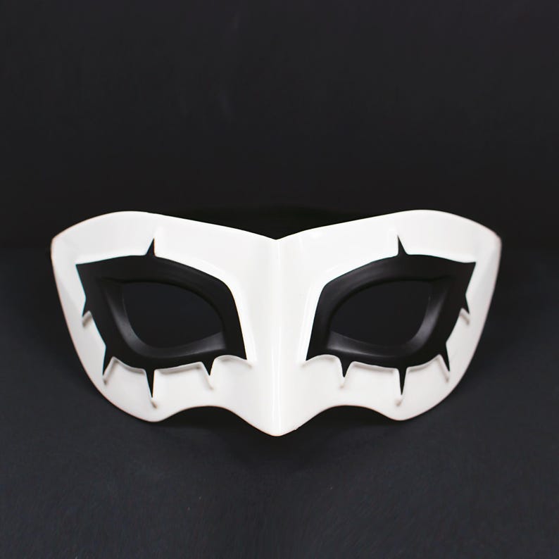 May include: A white mask with black eye coverings and sharp, pointed details. The mask has a smooth, glossy finish and is designed to cover the eyes and upper face. The mask is likely for costume or cosplay purposes.