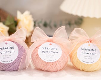 May include: Three skeins of VERALINE Puffie Yarn in pastel colors: lavender, peach, and yellow. Each ball is wrapped in a clear cellophane with a sheer pink bow and a tag with product details. Each skein is 50 g / 78 yds.