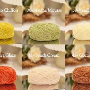 May include: A collection of six yarn skeins in various colors, including yellow, green, and orange. Each skein is labeled with a color name, such as "Mango Chiffon" and "Matcha Mousse". The yarn is displayed on a reflective surface.