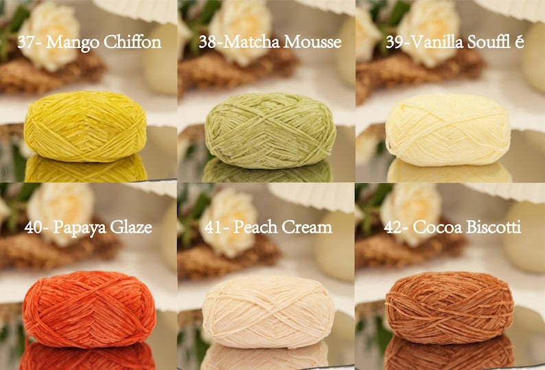May include: A collection of six yarn skeins in various colors, including yellow, green, and orange. Each skein is labeled with a color name, such as "Mango Chiffon" and "Matcha Mousse". The yarn is displayed on a reflective surface.