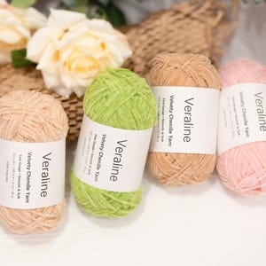 May include: Four skeins of Veraline velvety chenille yarn in shades of peach, green, tan, and pink. Each skein has a white label with the brand name and product details. The yarn is smooth and soft, perfect for knitting and crochet projects.