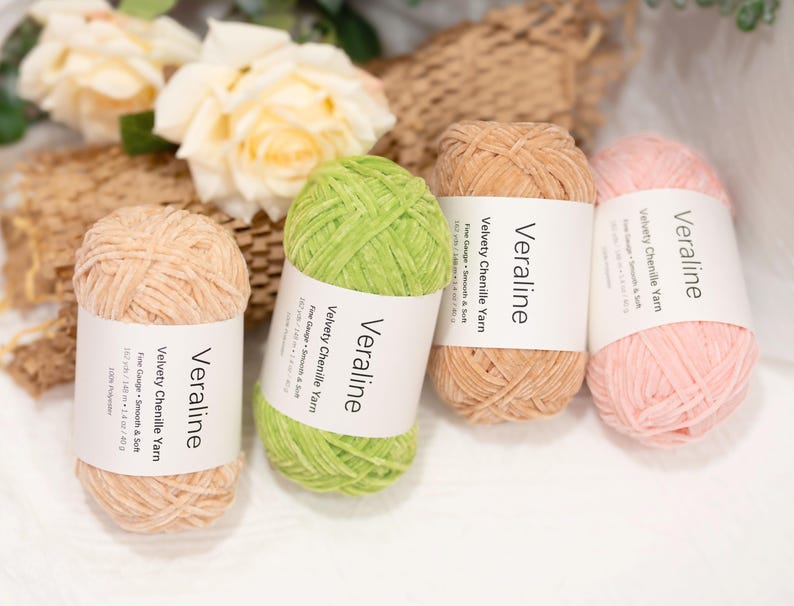 May include: Four skeins of Veraline velvety chenille yarn in shades of peach, green, tan, and pink. Each skein has a white label with the brand name and product details. The yarn is smooth and soft, perfect for knitting and crochet projects.