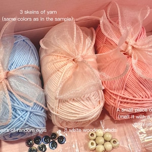May include: A craft kit for making a plush toy, containing three skeins of yarn in pink, light blue, and peach, four pairs of plastic eyes, eight white wooden beads, and a small package of hot glue.