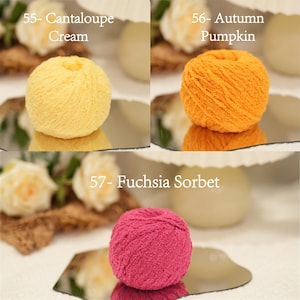 May include: Three balls of yarn in Cantaloupe Cream, Autumn Pumpkin, and Fuchsia Sorbet colours. Each ball is displayed on a reflective surface with text labels. The yarn is surrounded by decorative elements, including flowers.
