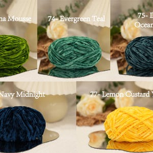 May include: A collection of velvet yarn balls in various colors, including green, teal, and navy. Each ball is labeled with a number and color name, such as "Matcha Mousse" and "Evergreen Teal". The yarn balls are displayed on mirrored surfaces.