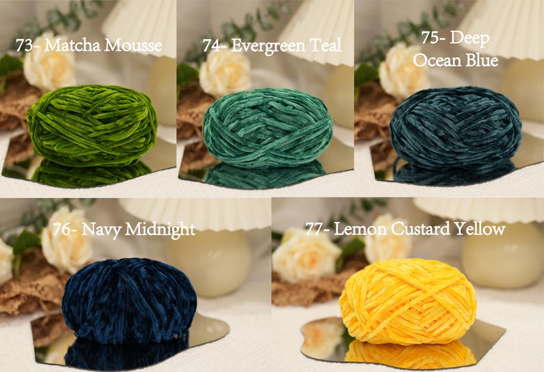 May include: A collection of velvet yarn balls in various colors, including green, teal, and navy. Each ball is labeled with a number and color name, such as "Matcha Mousse" and "Evergreen Teal". The yarn balls are displayed on mirrored surfaces.