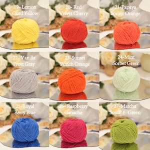 May include: A selection of nine balls of yarn in a variety of colours, including yellow, red, orange, grey, green, blue, and pink. Each ball is labelled with a colour name, such as "Lemon Curd Yellow" and "Raspberry Ganache."