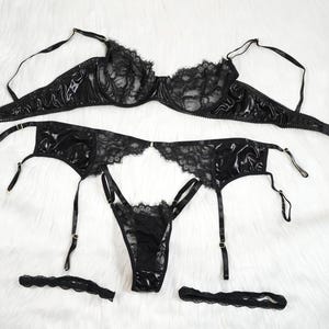 Könnte beinhalten: Schwarzes Dessous-Set mit einem Spitzen- und Satin-BH, einem Strumpfband und passenden Strumpfband-Trägern.