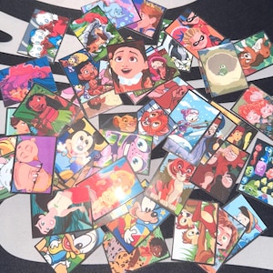 Op de afbeelding: Een verzameling kleurrijke, vierkante stickers met verschillende stripfiguren. De stickers tonen personages uit populaire animatiefilms en tv-programma's, met levendige kleuren en gedetailleerde illustraties. De stickers zijn verspreid over een zwart-wit patroon.