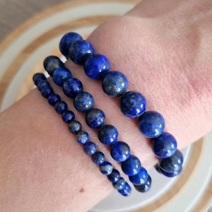 Peut inclure: Trois bracelets en perles de lapis-lazuli empilés sur le poignet d'une personne. Les bracelets sont faits de perles rondes bleu foncé.