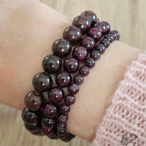 Op de afbeelding: Een stapel van vier armbanden gemaakt met donkerrode en bruine edelsteen kralen. De armbanden worden om de pols gedragen.