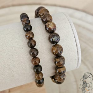 Peut inclure: Deux bracelets en perles brunes et noires avec un motif moucheté. Les bracelets sont sur une surface blanche.