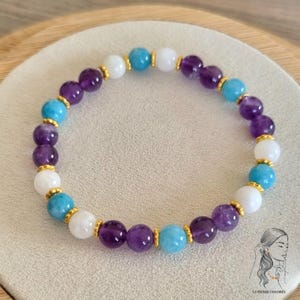 Op de afbeelding: Een armband gemaakt met amethist, turquoise en witte kralen. De kralen zijn geregen aan een gouden ketting.