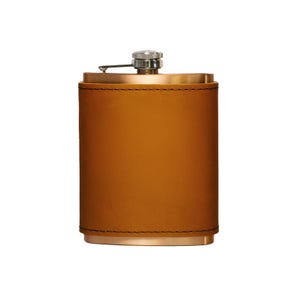 May include: A brown leather-wrapped flask with a silver cap and hinge. The flask has a rectangular shape with rounded edges and a stitched seam. The top and bottom are a metallic gold color.