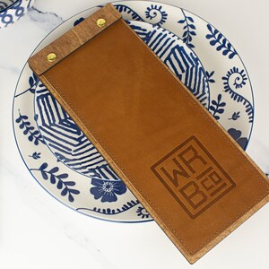 May include: A brown leather menu cover with a wooden backing and brass rivets. The cover has the text "WRB" embossed on the front.