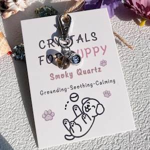 May include: A silver charm with a smoky quartz crystal and a paw print charm attached to a silver keyring. The charm is labelled "Crystals for Puppy" and "Smoky Quartz" and says "Grounding-Soothing-Calming".