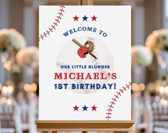 May include: A white sign on a wooden easel with baseball-themed graphics. The sign reads "WELCOME TO" above a baseball graphic with a bat, glove, and helmet. Below, it says "OUR LITTLE SLUGGER" and "MICHAEL'S 1ST BIRTHDAY!" Red and blue stars and baseball stitching decorate the sign.