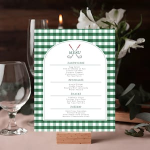May include: A green and white checkered menu card with a golf theme. The menu includes sandwiches, beverages, snacks, and desserts. The card is held in a wooden stand and features the word "MENU" at the top.