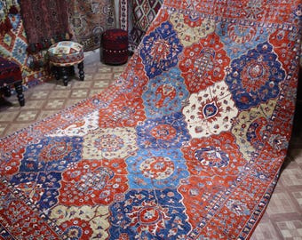 May include: A large, rectangular area rug with a patchwork design. The rug features a vibrant color palette of red, blue, beige, and cream. Intricate floral and geometric patterns adorn each patch, creating a visually rich and textured surface. The rug is likely made of wool.