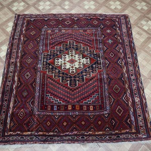 May include: A traditional Persian rug with a red, blue, and white geometric pattern. The rug has a central medallion and a border with intricate designs.