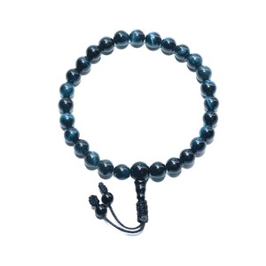 May include: A dark blue beaded bracelet with a black tassel and knot closure. The bracelet is made of round, polished beads. The beads are a deep blue color with subtle variations. The bracelet is displayed on a white background.