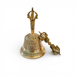 May include: A golden bell with intricate embossed patterns and a decorative handle. A matching golden scepter rests beside the bell. The bell and scepter are on a white background.