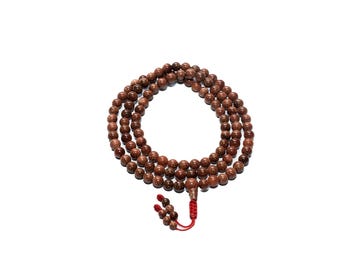 May include: A strand of brown beaded jewelry with a red tassel. The beads are a mix of brown and gold, creating a speckled appearance. The beads are strung together, forming a necklace or bracelet.