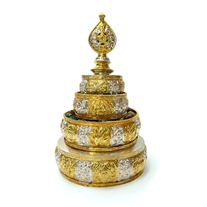 May include: An elaborate, tiered decorative item with gold and silver detailing. The base is a broad, circular form, with several smaller, stacked bowls above. The top features a decorative finial. The bowls have detailed relief patterns and are filled with small, colourful stones.