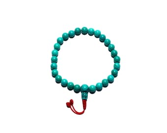 May include: Turquoise beaded bracelet with a red tassel. The bracelet features round, polished turquoise beads strung together. The red tassel is attached to the end of the bracelet. The bracelet is displayed on a white background.