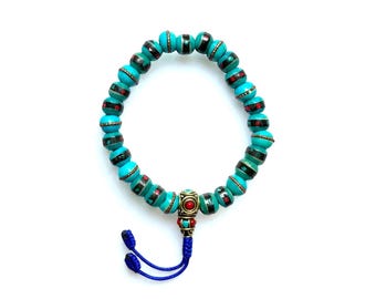 May include: Turquoise beaded bracelet with red and black accents. The bracelet features a decorative gold-colored centerpiece with red and black details, and a blue tassel.