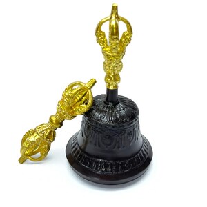 May include: A black and gold Buddhist bell with a detailed design. The bell has a gold handle and a matching gold dorje, a ritual object. The bell is approximately 5 inches tall.