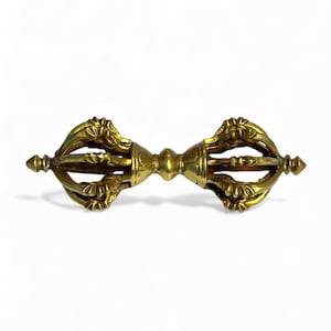 May include: A gold-coloured vajra, a ritual object with ornate floral designs. The vajra has a central sphere and pointed ends, with intricate details throughout. It is a symmetrical, handheld item.