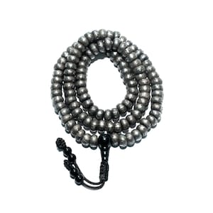 Puede incluir: Un collar o rosario de cuentas plateadas, sobre un fondo blanco. Las cuentas son redondas y espaciadas uniformemente, con una borla negra y una cuenta negra más grande en el extremo.