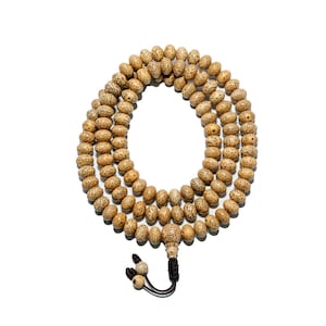 May include: A strand of prayer beads made of light brown, speckled seeds. The beads are strung together in multiple loops, with a black tassel and decorative beads at the end. The background is plain white.