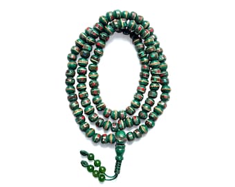 Puede incluir: Un collar de cuentas verdes con detalles rojos y dorados. Las cuentas están ensartadas, formando múltiples hebras. Una borla verde cuelga de la parte inferior. El fondo es blanco.