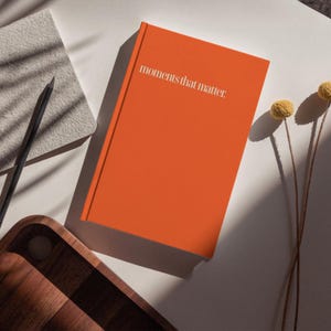 May include: An orange journal with the text "moments that matter" printed in white on the cover.