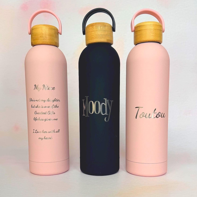 Three personalised insulated water bottles with engraved names and message text, shown in blush pink and black with bamboo-effect lids. Custom reusable bottles for personal gifts, branded giveaways or company merchandise.