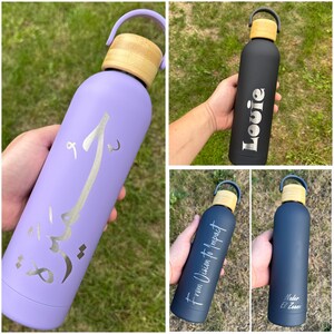 Four personalised bamboo-lid water bottles in black, navy, and lilac. Custom engraved with names, Arabic script, or phrases like “From Vision to Impact.” Reusable insulated bottles ideal for corporate gifts, daily hydration, or personal use.
