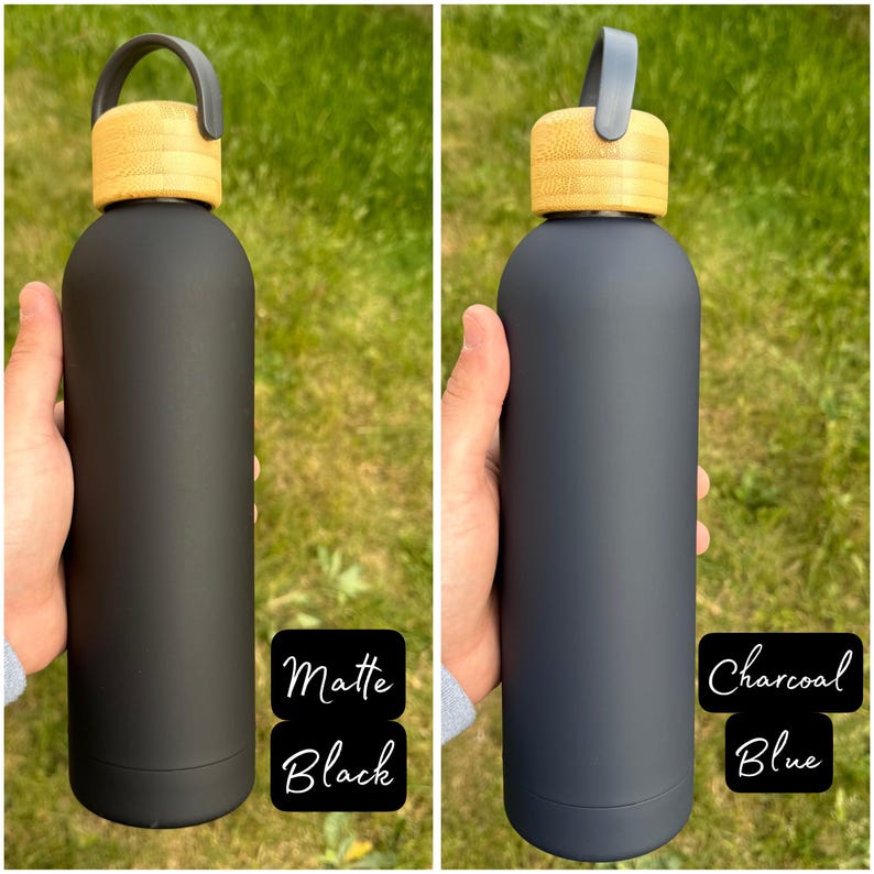 Side-by-side image of two darker-toned water bottles held outdoors. The left bottle is Matte Black with a bamboo lid and black loop handle. The right bottle is a deep Charcoal Blue, also with a bamboo lid and coordinating dark blue handle.